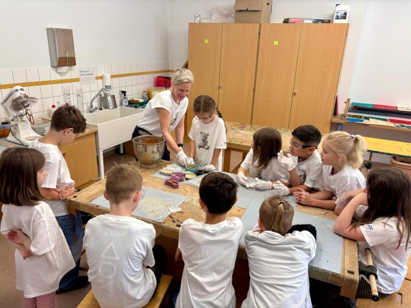 Eine Gruppe Kinder arbeitet mit einer Erwachsenen an einer Betonfigur.