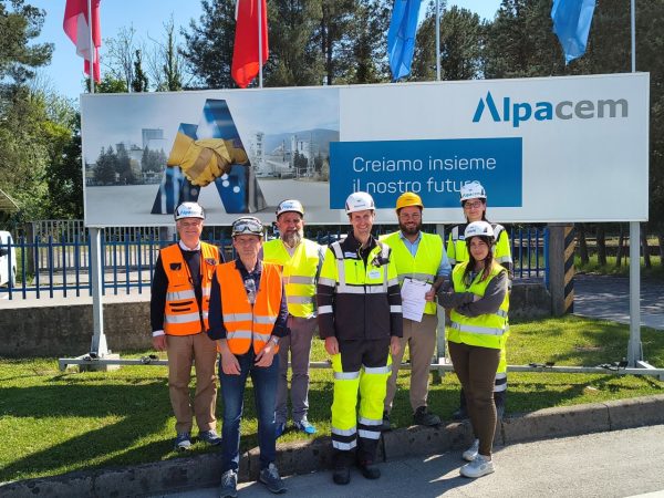 Eine Gruppe Menschen in Schutzkleidung vor einem Alpacem-Schild