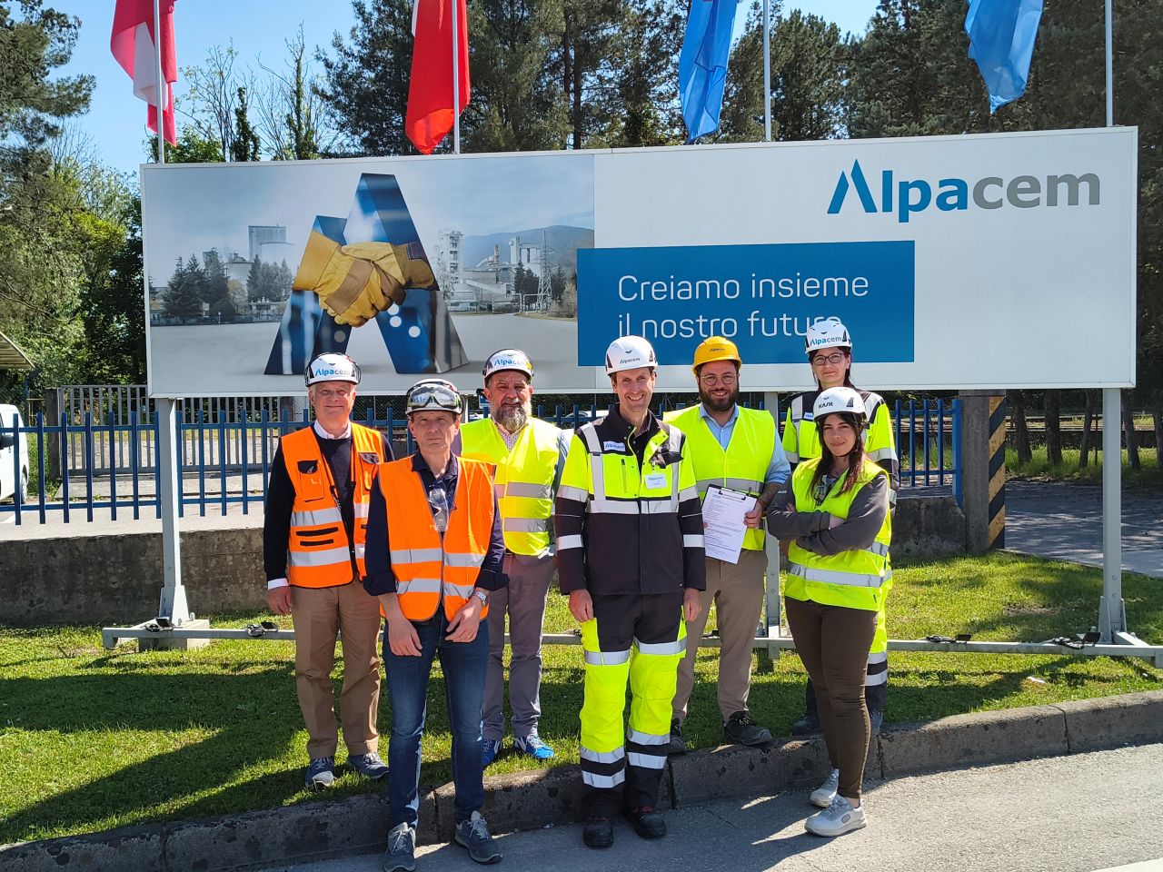 Eine Gruppe Menschen in Schutzkleidung vor einem Alpacem-Schild