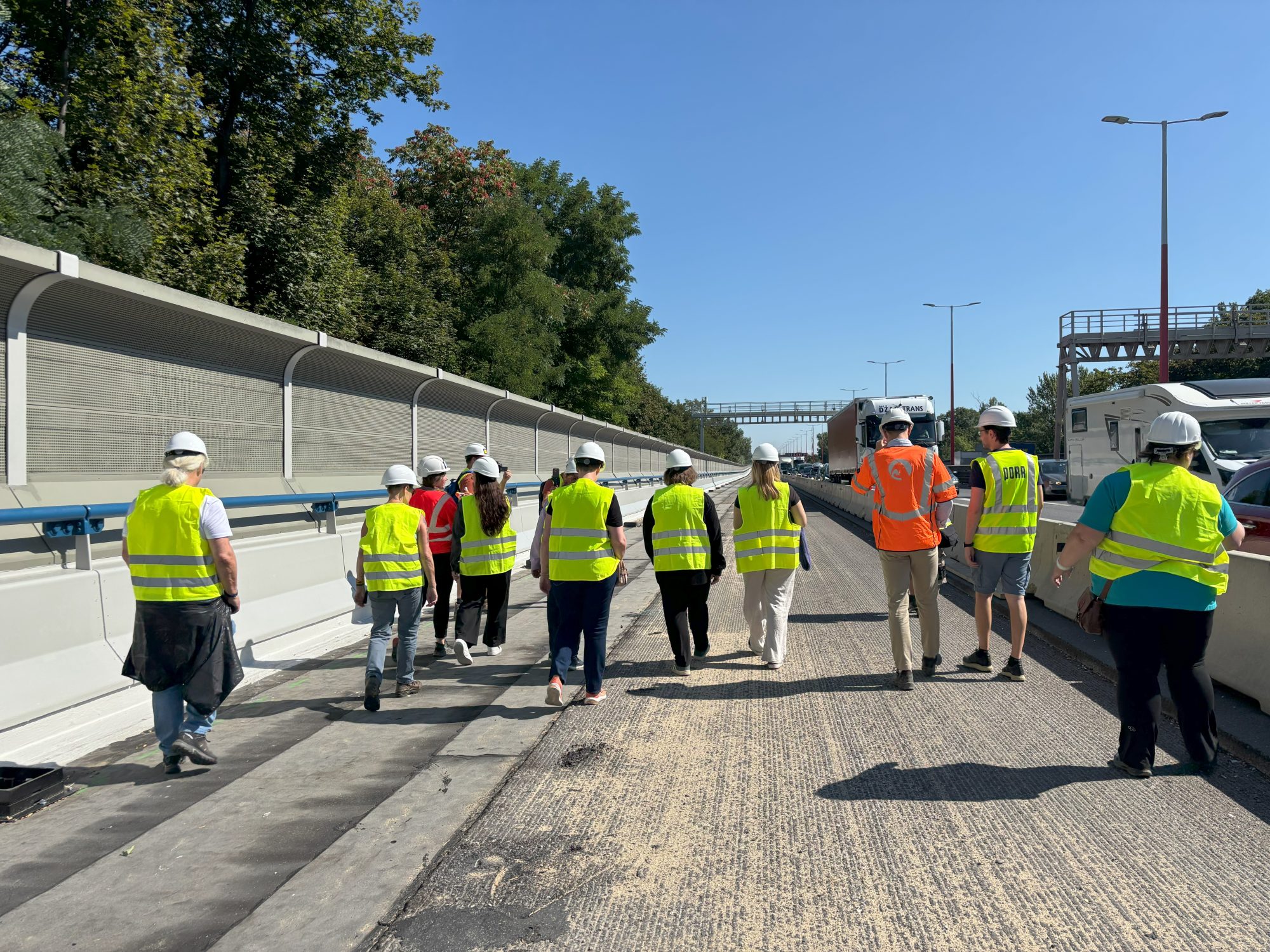 Eine Gruppe Menschen in gelben Schutzwesten und Helmen geht auf einer Baustelle