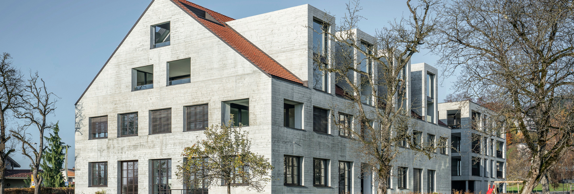 Wohnanlage Wiesenweg in Wolfurt mit skulpturaler Sichtbetonfassade an Bestand und Neubau