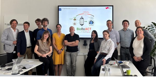 Gruppenfoto vor einem Bildschirm auf dem BioREACT steht