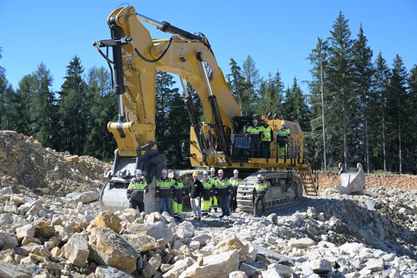 Ein großer Bagger arbeitet in einem Steinbruch davor steht eine Gruppe Menschen