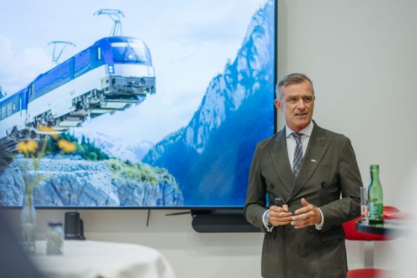 Ein Mann steht vor dem Bild eines Zuges der scheinbar in der Luft fährt, da Schienen und Beton fehlen