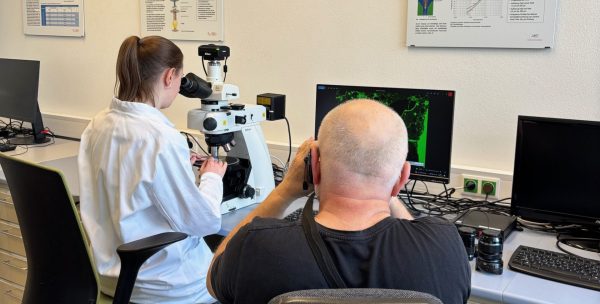 Junge Frau am Mikroskop wird von einem Mann fotografiert.