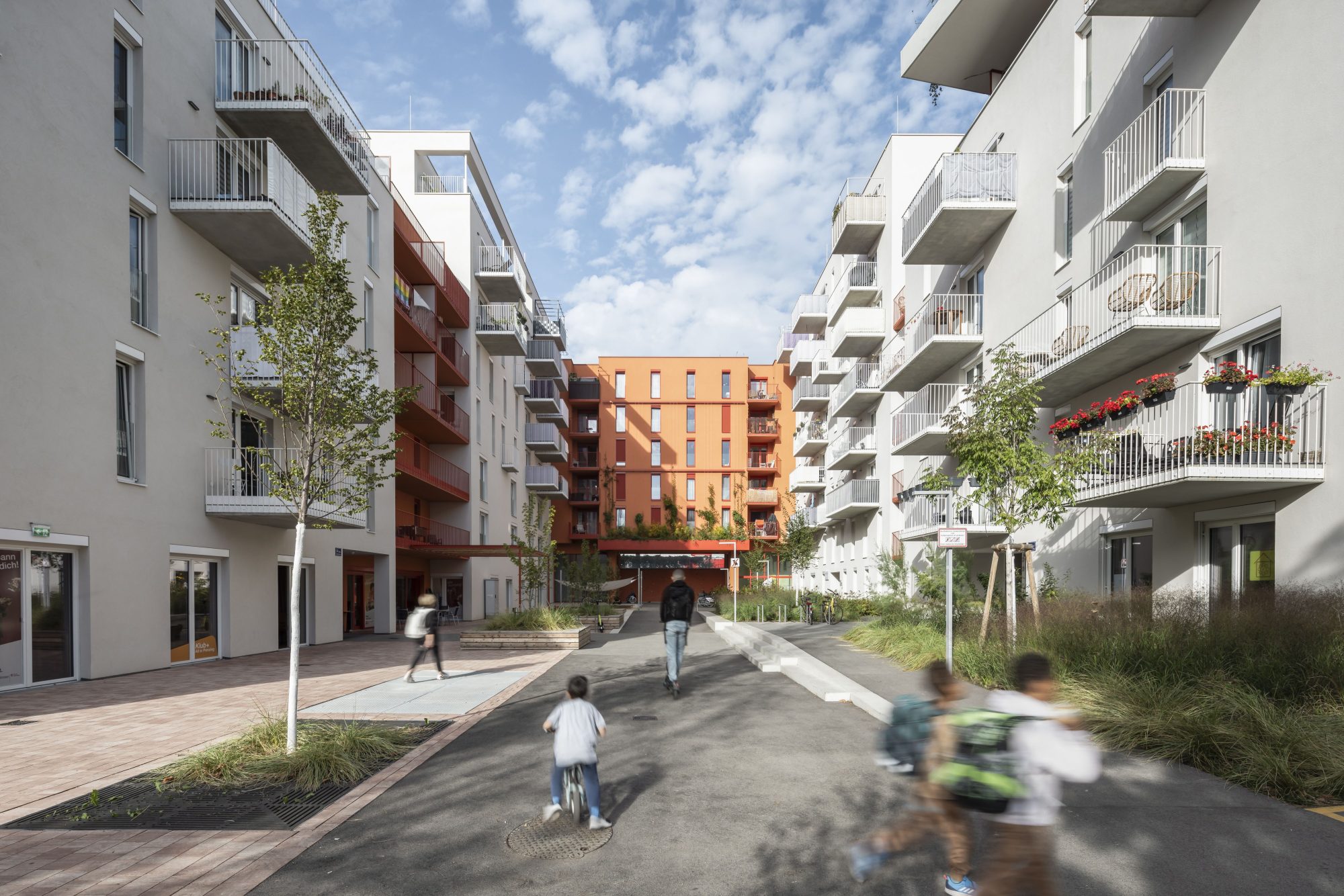 Innenhof des Wohnquartiers Wientalterrassen mit spielenden Kindern, ein Vorzeigebeispiel für Bauteilaktivierung. Die Fassade der Gebäude sind hellgrau und teils orange.